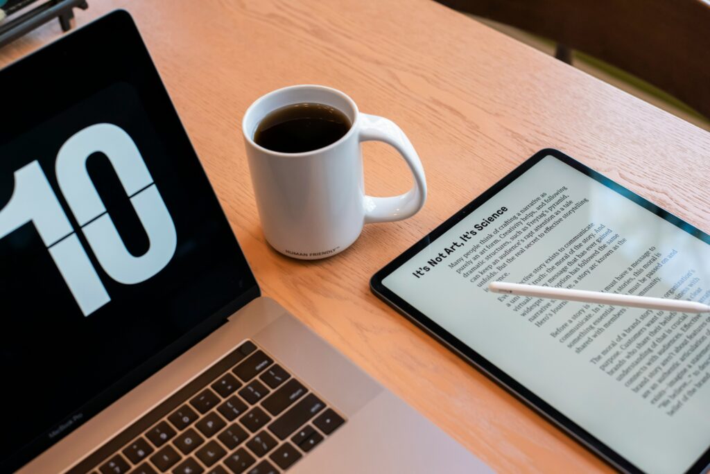 A laptop with a clock, a cup of coffee, and a tablet open to an eBook.