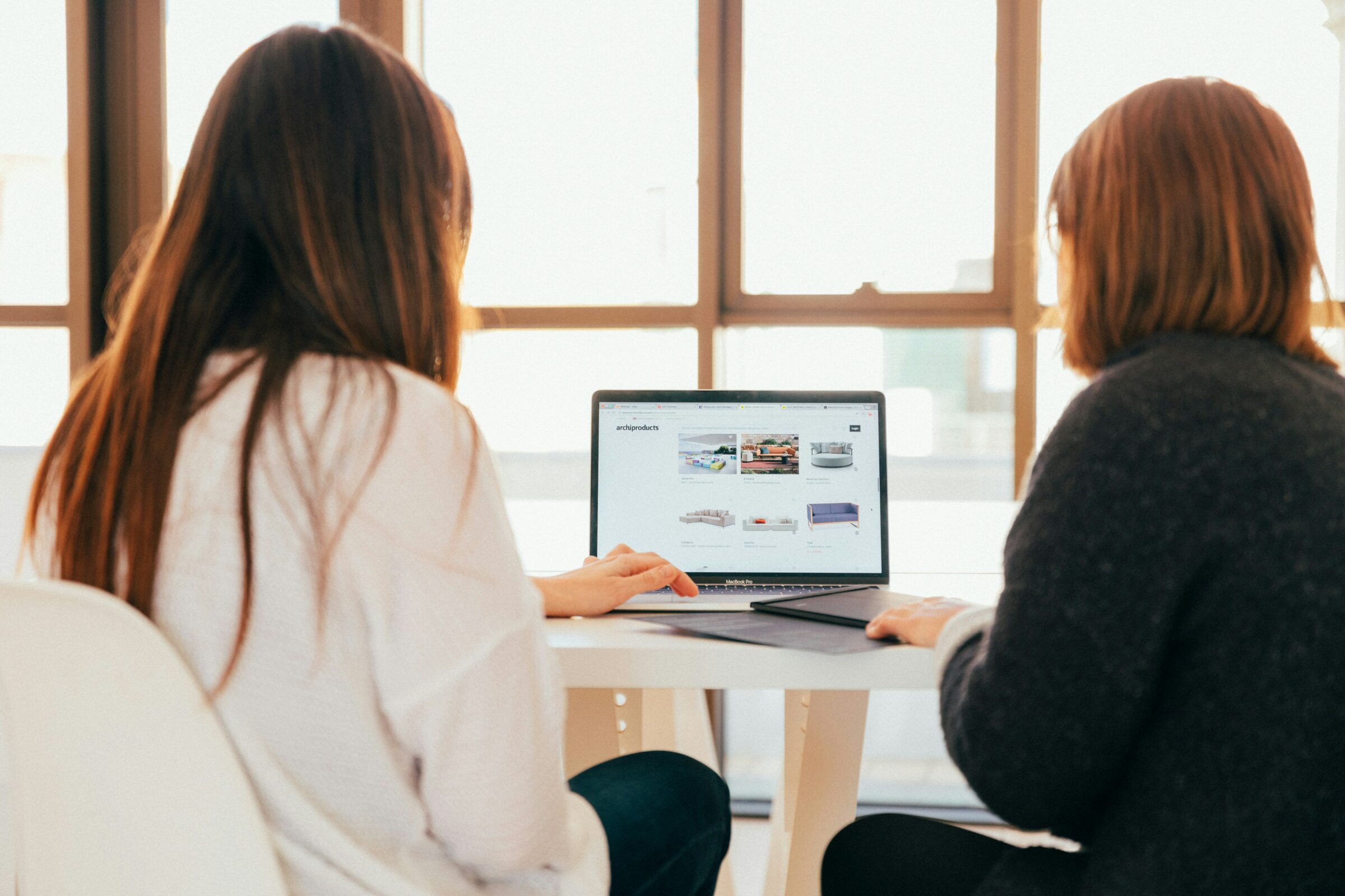 Two women look at email marketing on a laptop.