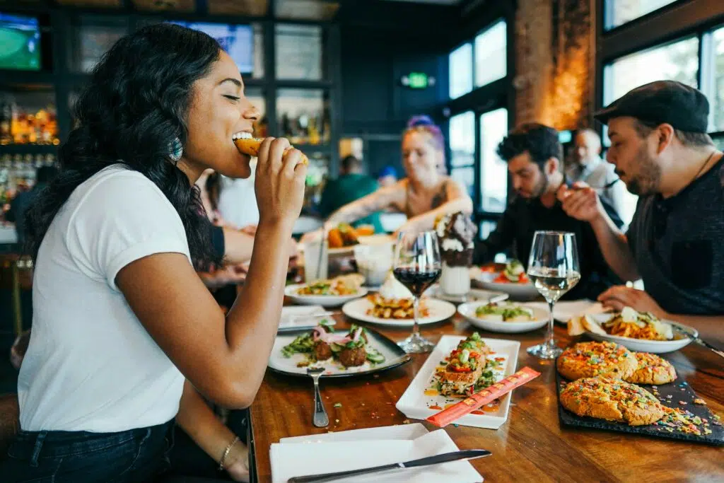 A woman eating an appetizer at a local restaurant with her friends in the backgroudn.